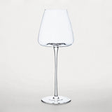 An empty clear wine glass with a tapered bowl, slender stem, and round base stands against a pale background.