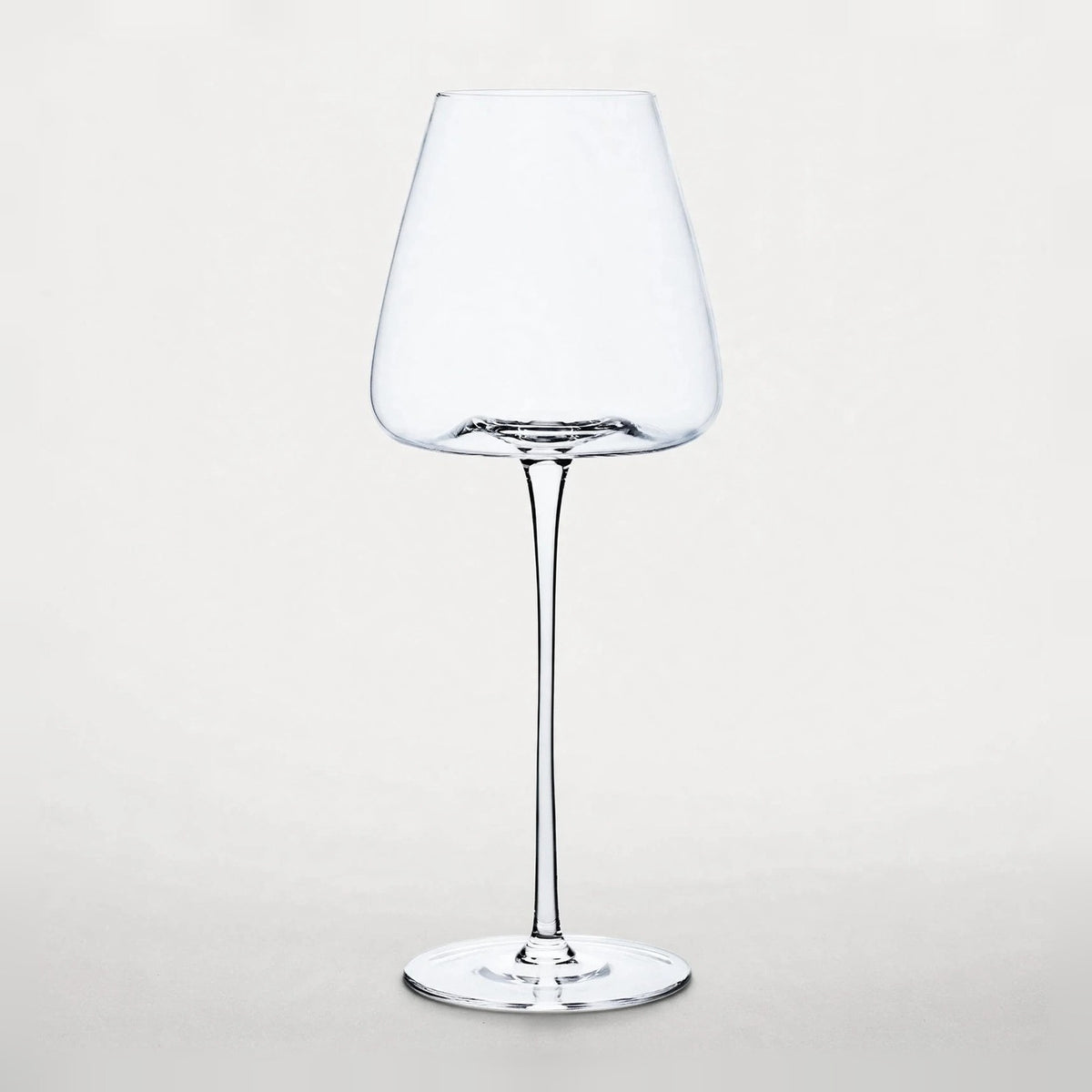 An empty clear wine glass with a tapered bowl, slender stem, and round base stands against a pale background.
