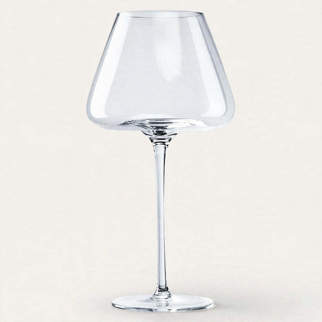 An empty clear wine glass with a broad angular bowl and tall slender stem stands against an off-white background.