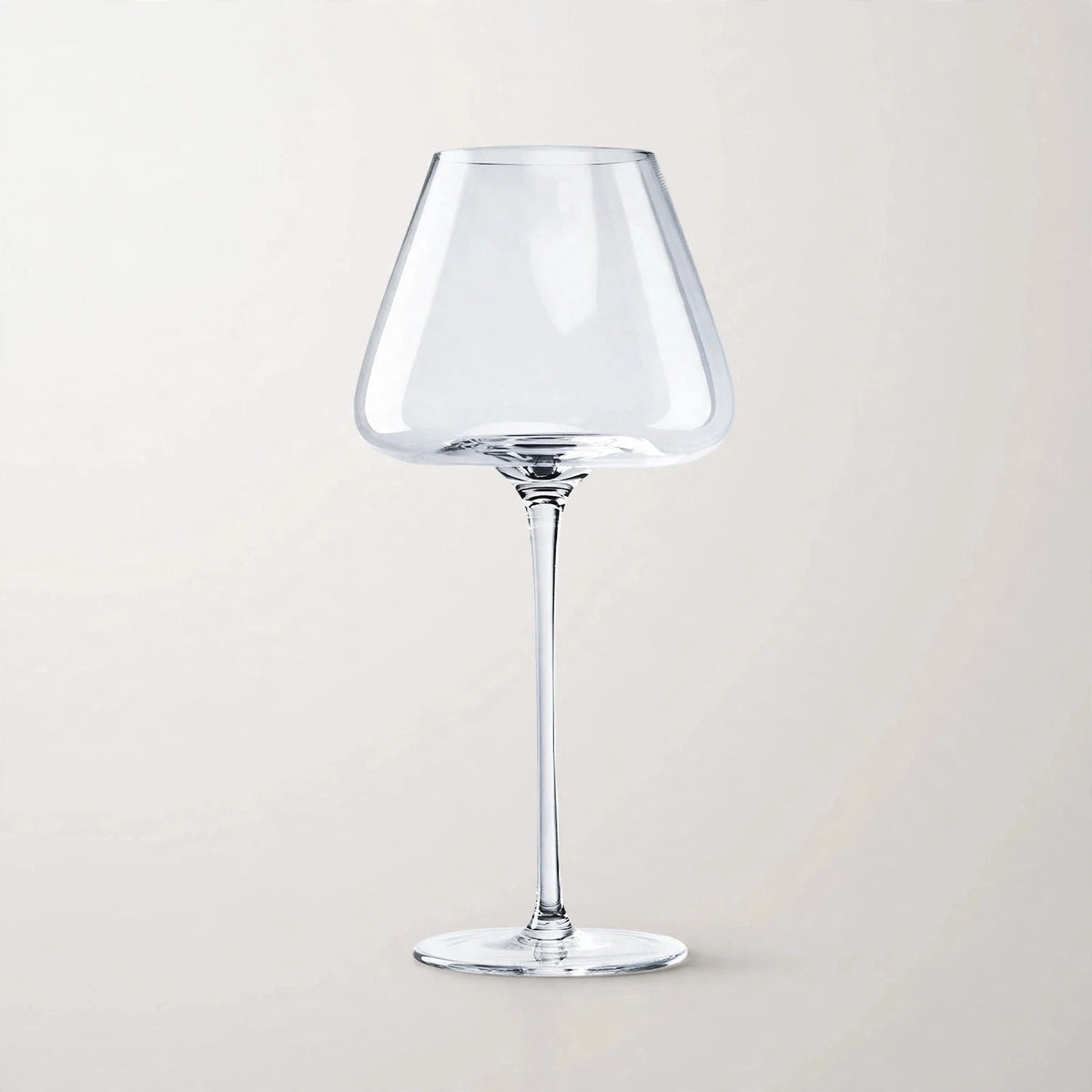 A single empty clear wine glass with a wide tapered bowl, slender stem, and circular base stands against a pale background.