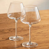 Two empty clear wine glasses with tapered bowls and tall stems stand diagonally apart on a wooden table.