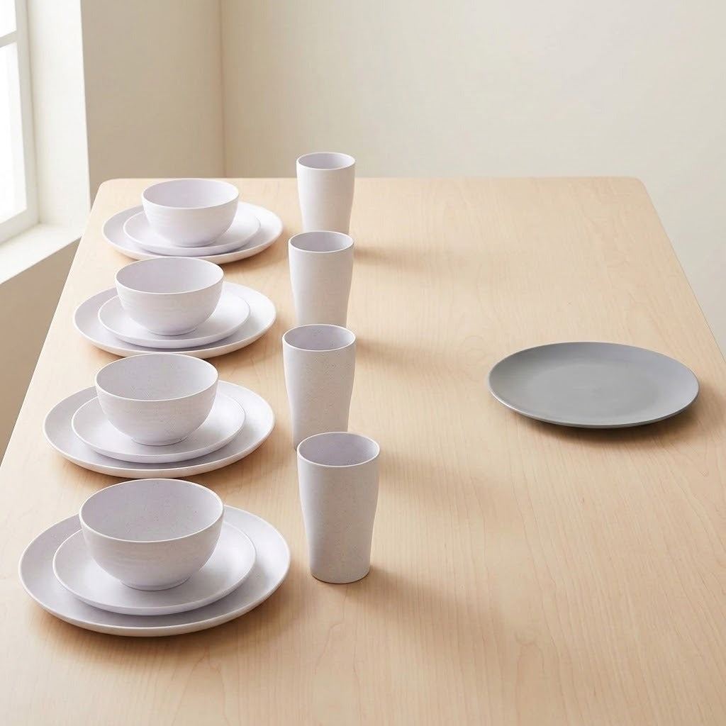 Four white place settings with bowls, plates, and tall cups line a wooden table beside a window, with an extra plate nearby.