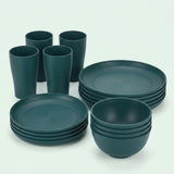 Dark green dinnerware includes four tall cups and stacks of large plates, smaller plates, and bowls against a pale background.