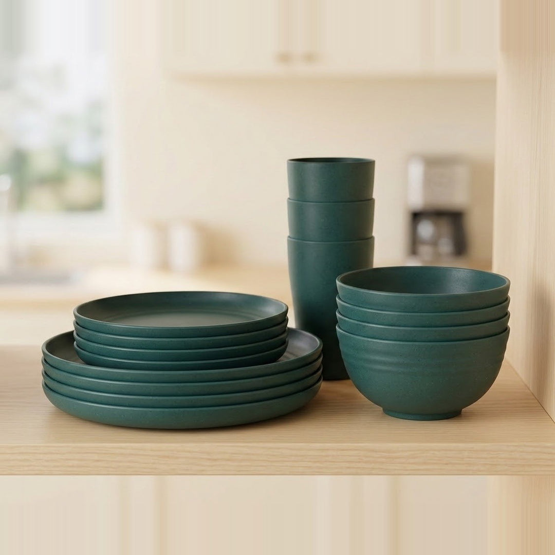 Dark green dinner plates, smaller plates, bowls, and cups are stacked on a light wooden shelf in a bright kitchen.