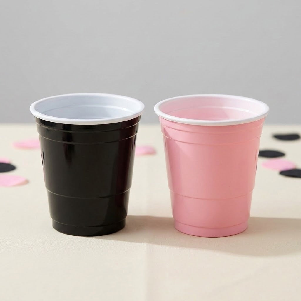 A black cup and a pink cup with white rims stand side by side on a pale table scattered with matching confetti.