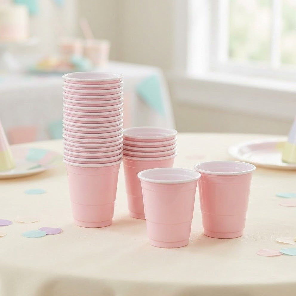 Two stacks of pink cups with white rims stand beside two separate cups on a pale table scattered with pastel confetti.