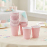 Two stacks of pink cups with white rims stand beside two separate cups on a pale table scattered with pastel confetti.