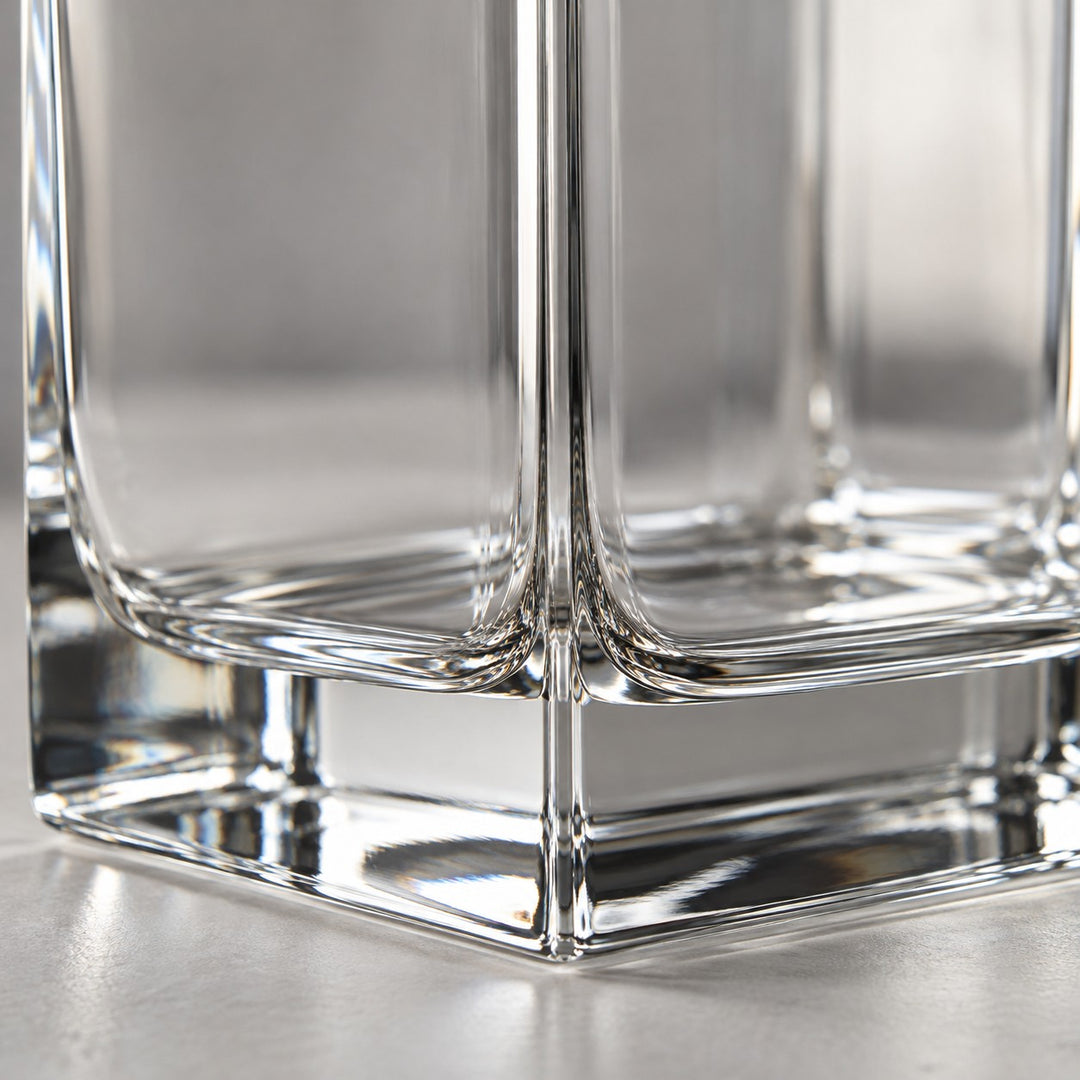 A macro view shows the smooth clear glass corner and thick polished base of the square decanter.