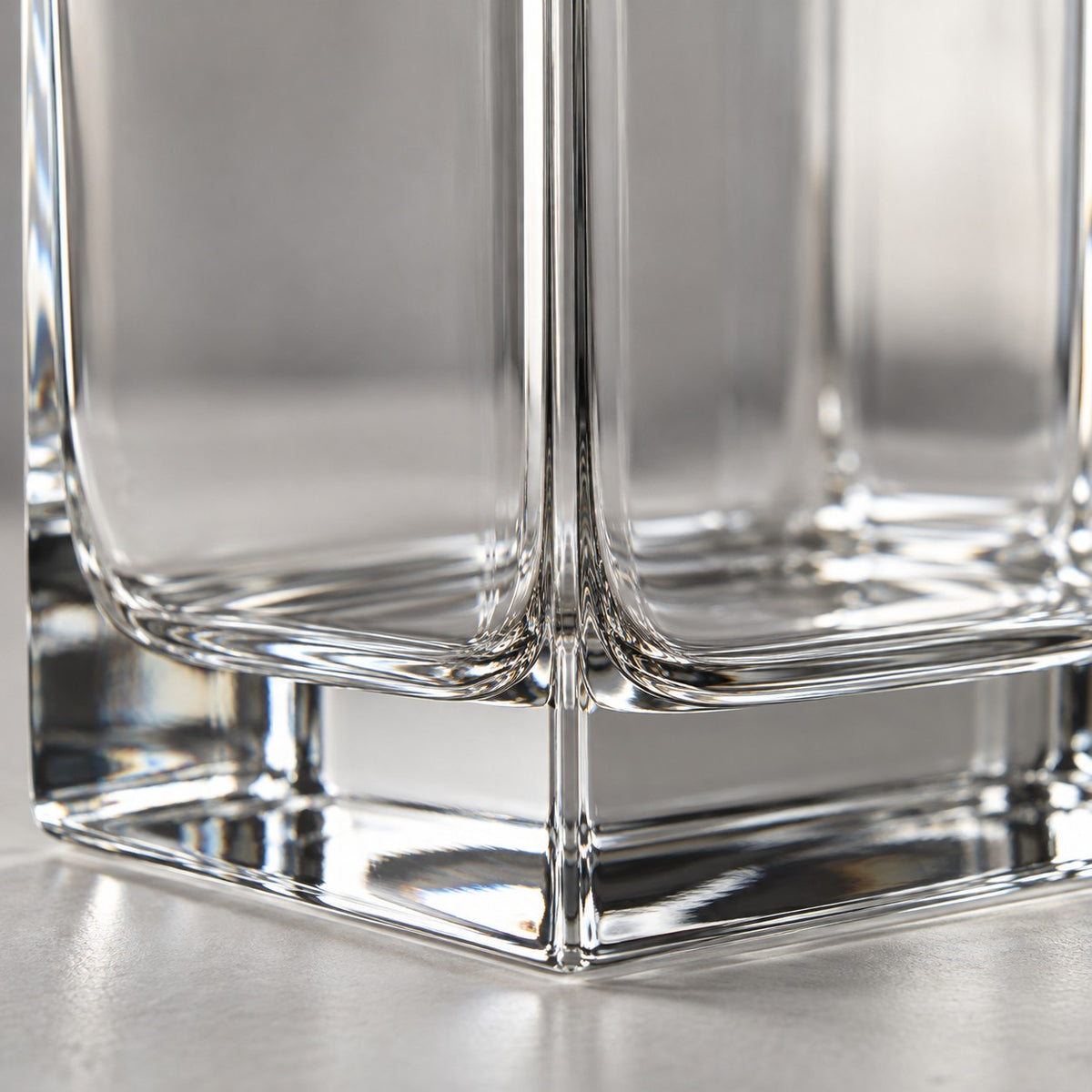 A macro view shows the smooth clear glass corner and thick polished base of the square decanter.