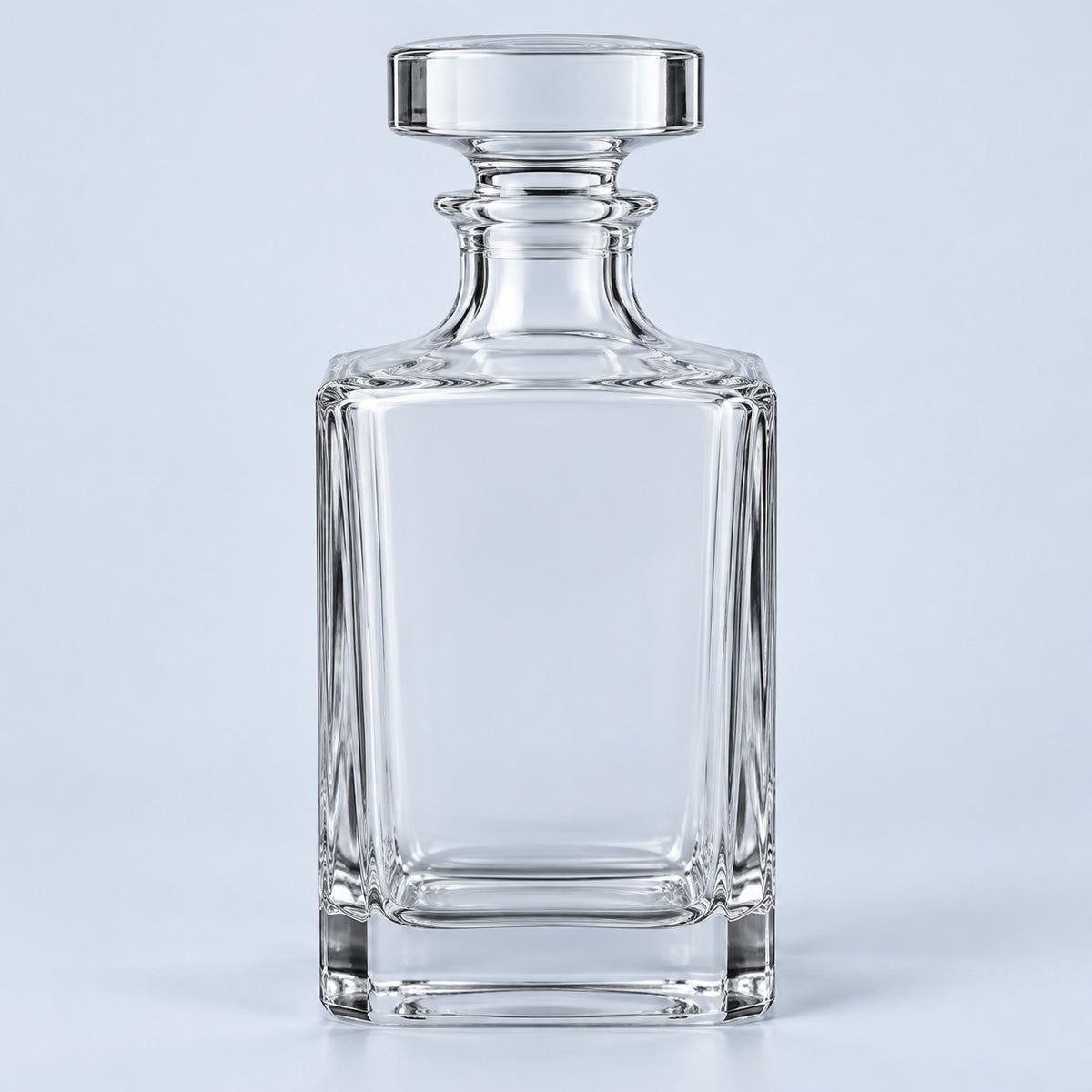 The clear smooth square glass decanter with its broad stopper stands against a pale blue backdrop.