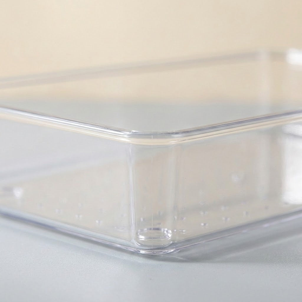 A clear plastic rectangular storage container with a perforated bottom, shown on a light gray surface against a beige background.