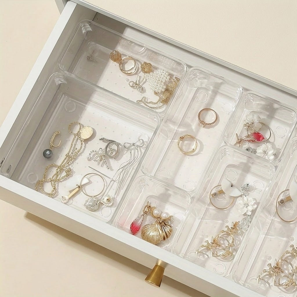 Clear plastic drawer organizer trays arranged inside an open white drawer, holding assorted rings, necklaces, earrings, and bracelets.