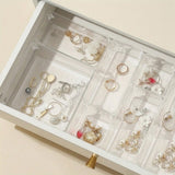 Clear plastic drawer organizer trays arranged inside an open white drawer, holding assorted rings, necklaces, earrings, and bracelets.