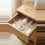 Clear plastic drawer organizer trays arranged inside an open wooden drawer, holding eyeglasses, a mouse, earphones, cables, and a small rectangular item. A matching clear tray sits on the wooden bedside table above.