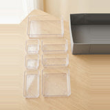 Six clear plastic rectangular storage boxes in different sizes arranged on a light wood table next to a gray box.