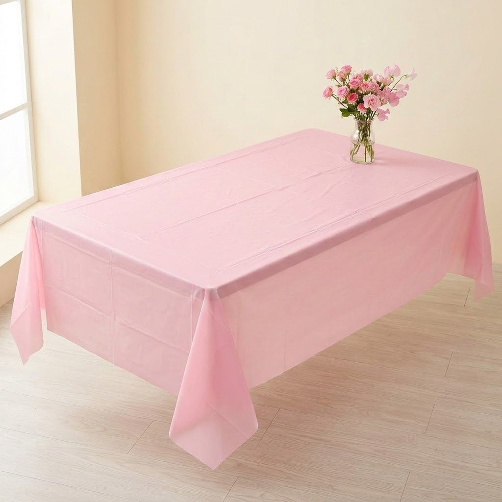 A light pink plastic tablecloth draped over a rectangular table in a bright room, with a small vase of pink flowers placed on top.