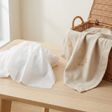 A white plastic tablecloth rests on a wooden table beside an open wicker basket draped with a stained beige cloth.