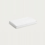 A neatly folded stack of white fabric sheets or a bedding set, photographed on a clean, solid, very light off-white background.