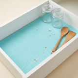 A square white drawer organizer tray with a light blue textured non-slip mat, shown with two clear glass jars and two wooden spoons inside on a beige background.