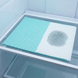 A rectangular dual-sided refrigerator moisture control mat shown inside a freezer shelf. The left side is a textured light aqua blue non-stick surface with water droplets, and the right side is a white paper towel showing a dark gray absorbed stain.