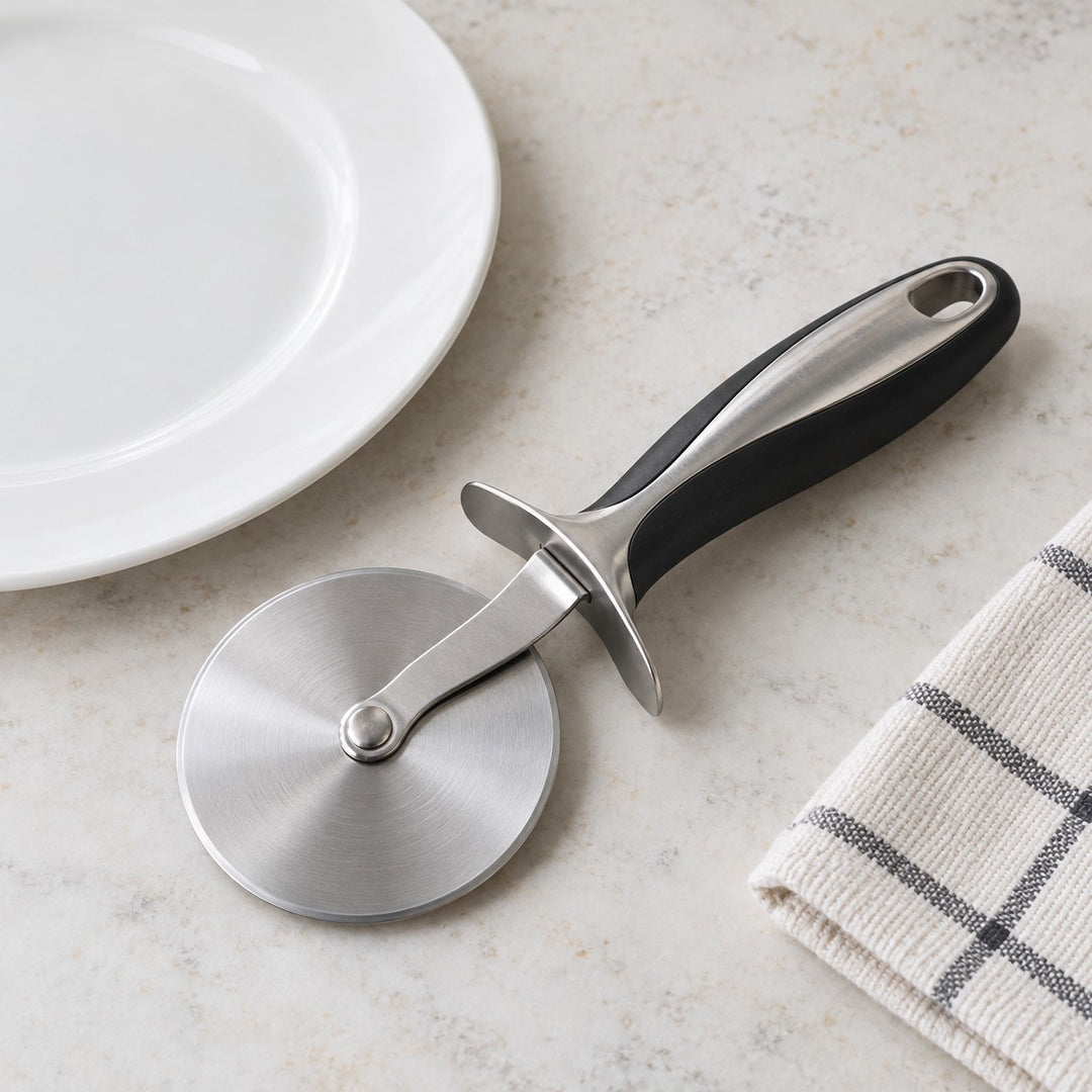 Pizza cutter wheel beside a dinner plate shows its compact handheld size on a countertop.