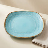 A light blue ceramic serving platter with a gold rim and white dotted decorative patterns, shown on a neutral beige surface next to a folded beige cloth.