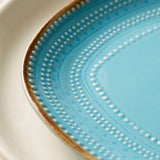 Close-up of a light blue ceramic plate with concentric dotted patterns and a brown rim, layered over a white plate.