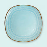 A light blue ceramic serving platter with a rounded square shape, decorated with concentric bands of white dots and a thin brown rim, shown against a solid pale mint green background.