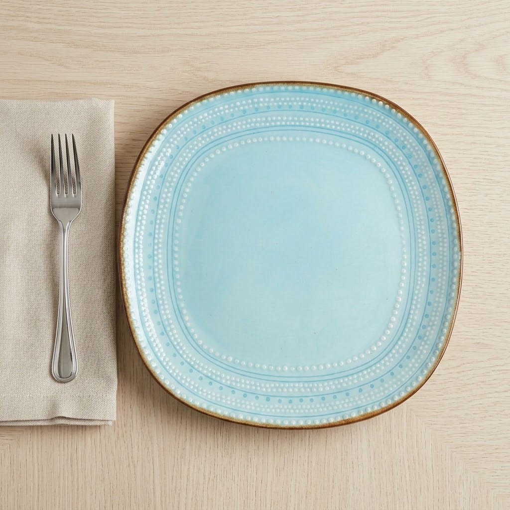 Turquoise ceramic plate with embossed dotted detailing and a brown rim beside a fork and linen napkin on a wooden table.