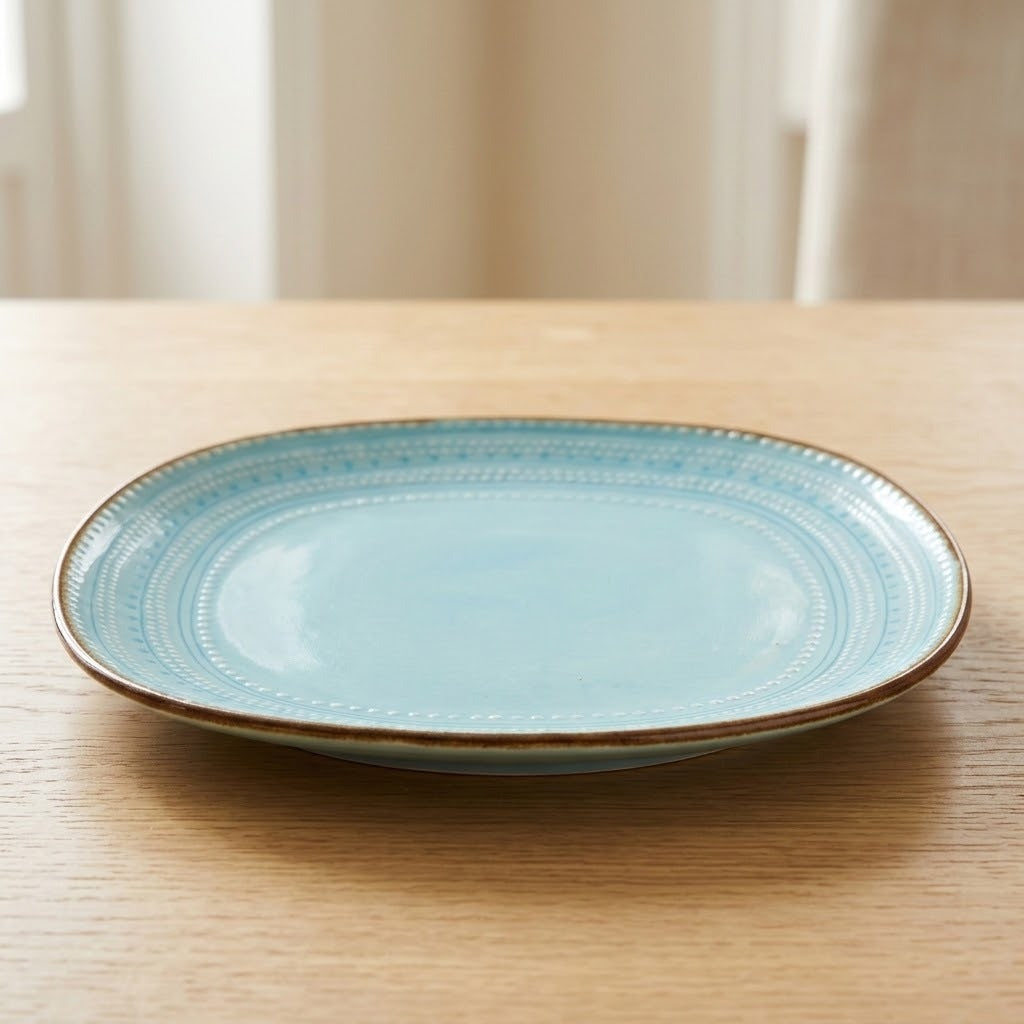 Turquoise ceramic plate with embossed detailing and a brown rim viewed from a low angle on a wooden table.
