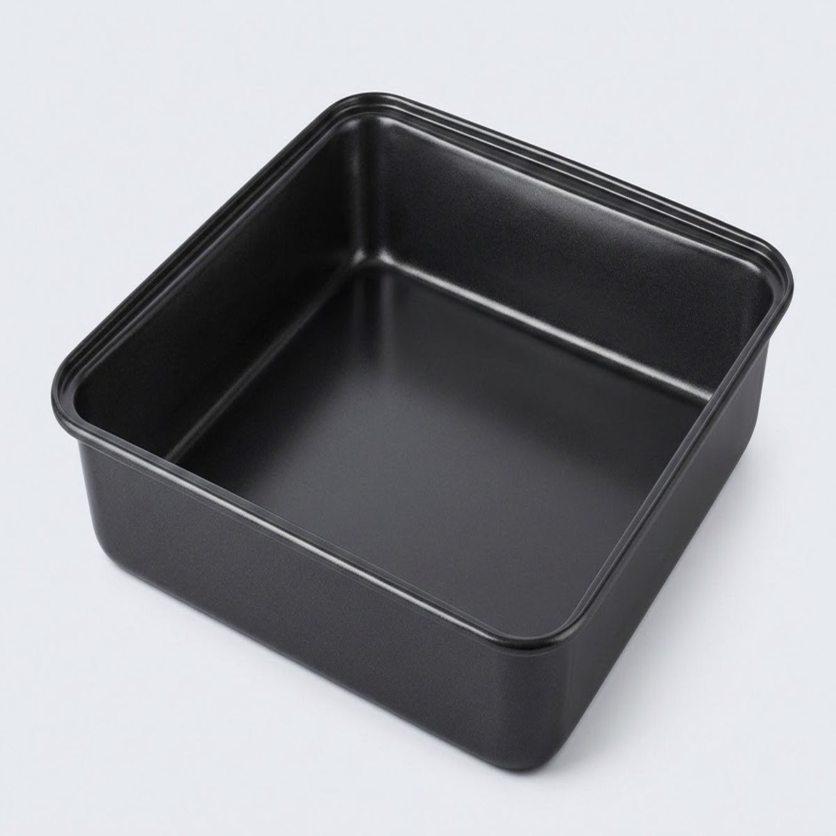 A square black non-stick baking pan with raised rim edges, photographed from an elevated angle on a light gray background.