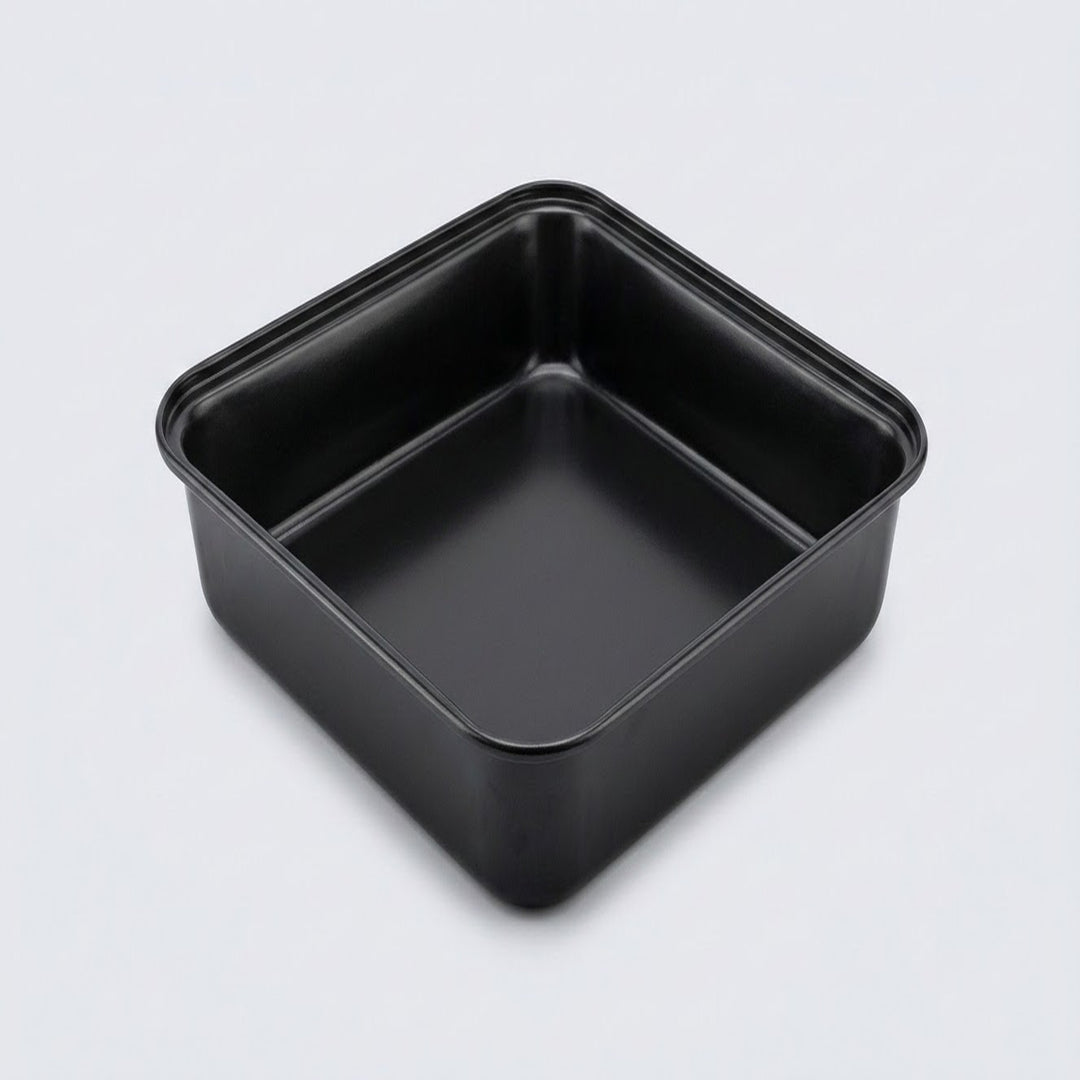 A square black non-stick baking pan with a raised rim and a single center divider, shown from an elevated perspective on a light gray background.