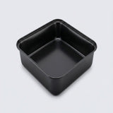 A square black non-stick baking pan with a raised rim and a single center divider, shown from an elevated perspective on a light gray background.