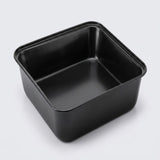 A square black non-stick baking pan with a low profile and raised rim, shown from an elevated perspective on a light gray background.