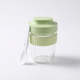 A clear glass jar with a light green lid and matching green ribbed band, shown on a white background with a small white spoon resting against the side.