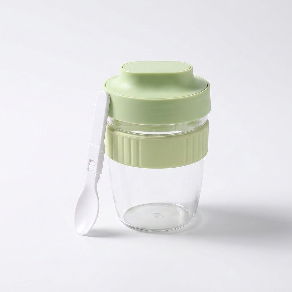 A clear glass jar with a light green lid and matching green ribbed band, shown on a white background with a small white spoon resting against the side.
