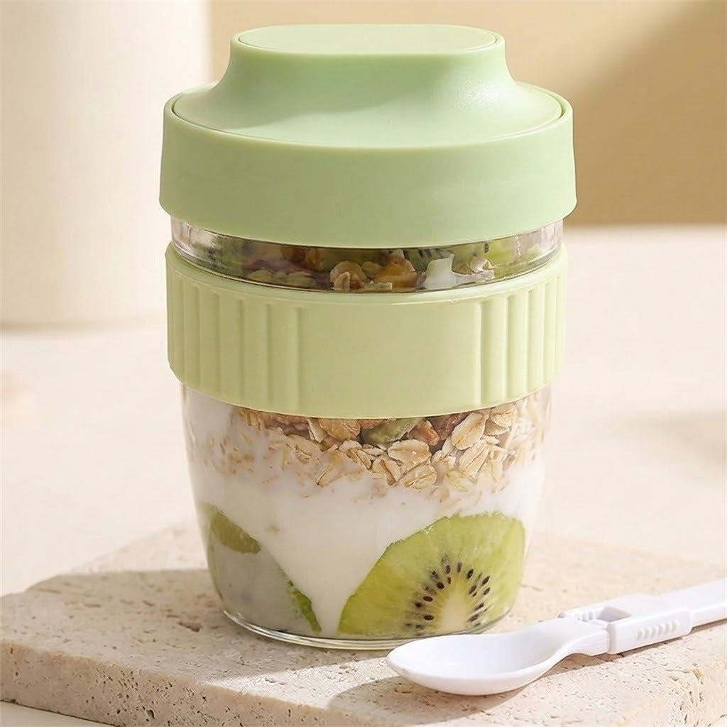 A portable personal blender bottle with a light green lid and ribbed base, filled with yogurt, oats, and kiwi slices, sitting on a stone surface next to a white spoon.
