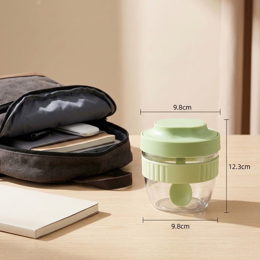 A small reusable glass jar with a light green lid and matching green inner scoop, shown on a wooden table beside an open gray bag and notebook. White dimension lines and text label the jar's height and width as 12.