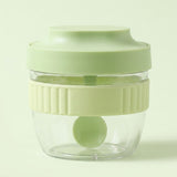 A small clear plastic food chopper jar with a light green lid and a pale yellow-green ribbed handle band, shown on a light green background.