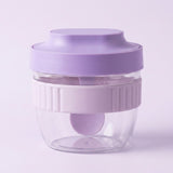 A small travel coffee maker with a lavender purple lid, a ribbed translucent white middle band, and a clear plastic bottom cup, shown on a light lavender background.