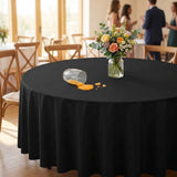 A round black tablecloth draped over a round table in a bright event hall, with a floral centerpiece and a tipped-over clear glass with orange liquid spilled on the table surface. Blurred people and chairs are visible in the background.