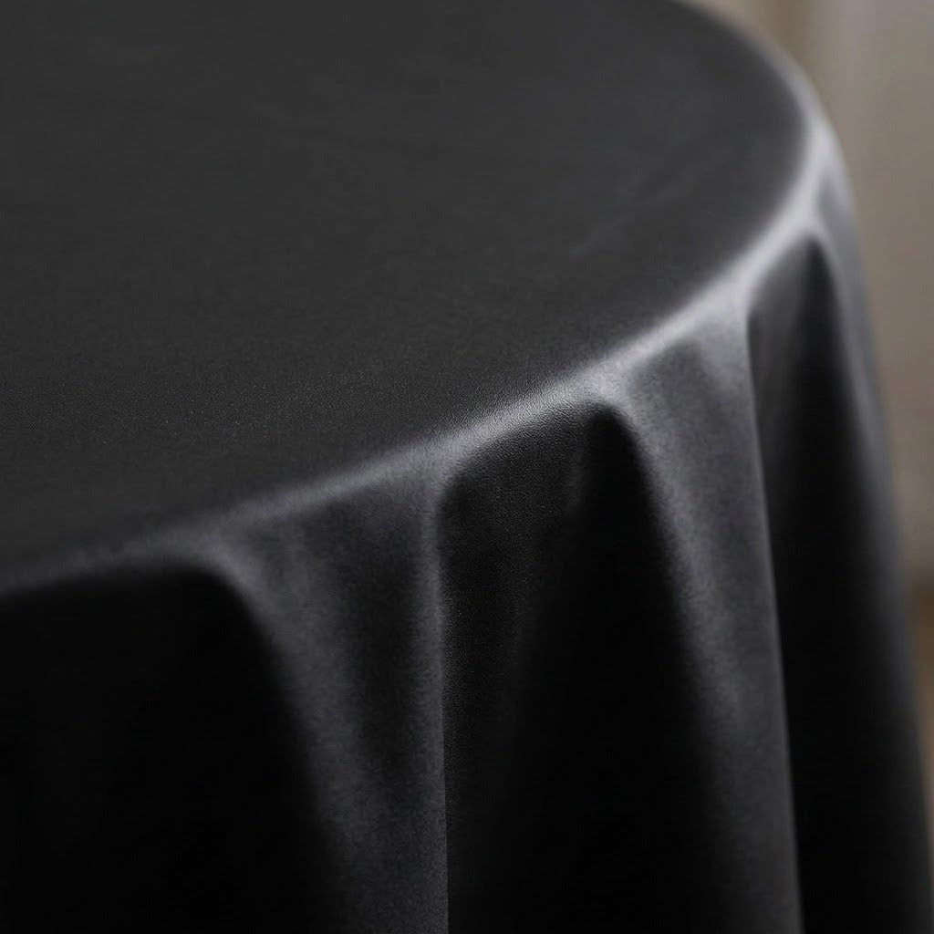 A close-up of a black tablecloth draped over a round table, showing the smooth fabric texture and soft folds.