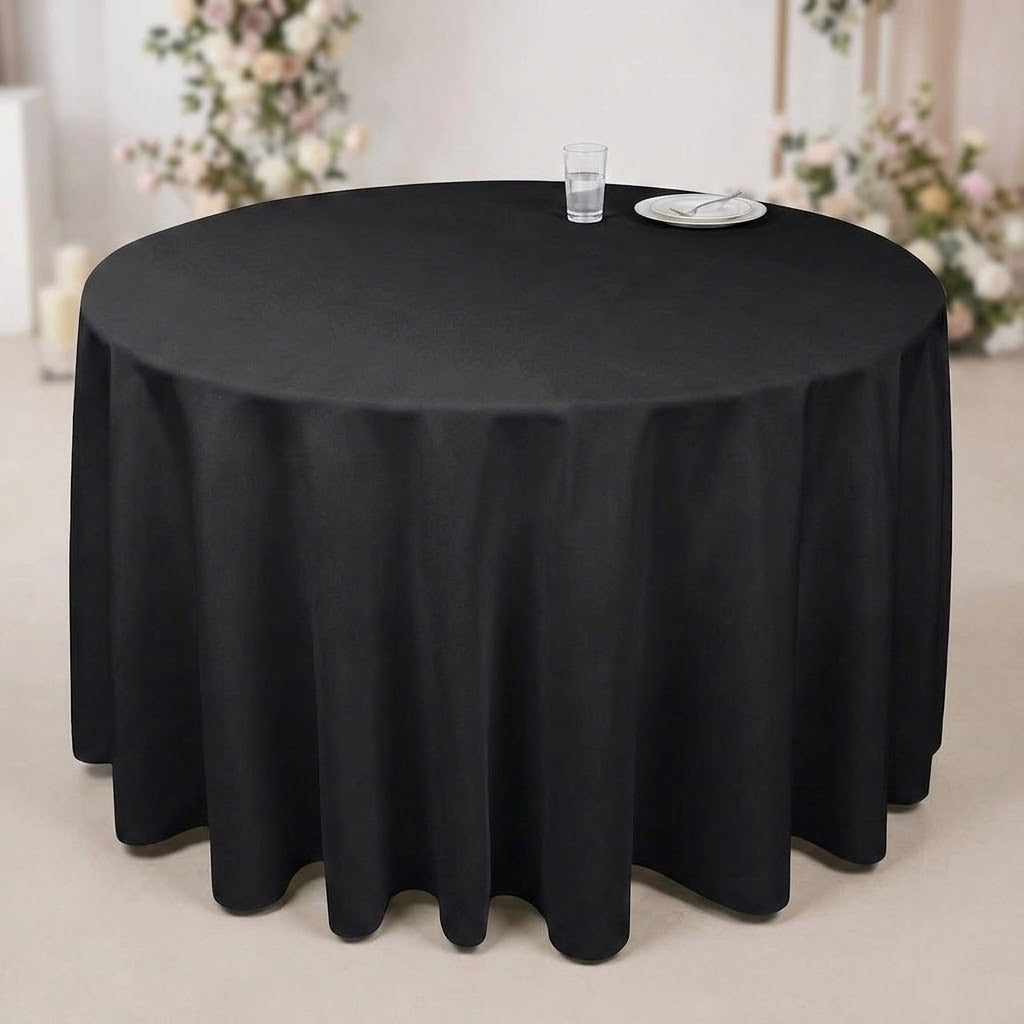 A round black tablecloth draped over a round table, with a small glass and plate on top, set in an indoor event space with blurred floral decorations in the background.