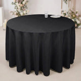 A round black tablecloth draped over a round table, with a small glass and plate on top, set in an indoor event space with blurred floral decorations in the background.