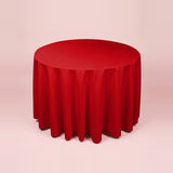 A round red tablecloth draped over a round table, shown against a solid pale pink background.