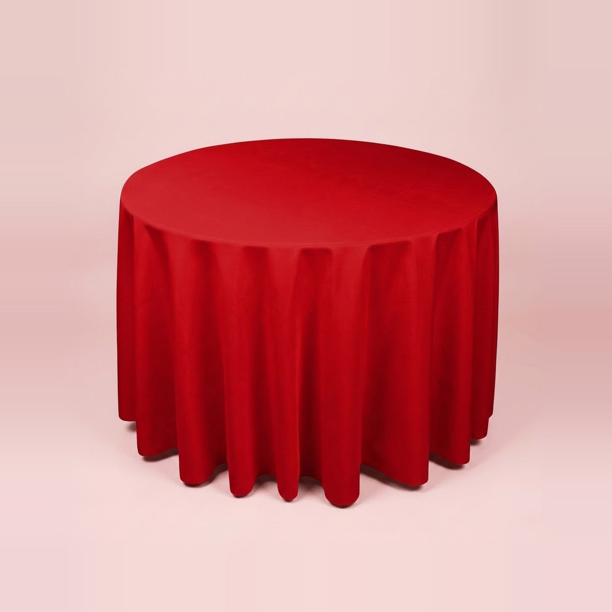 A round red tablecloth draped over a round table, shown against a solid pale pink background.