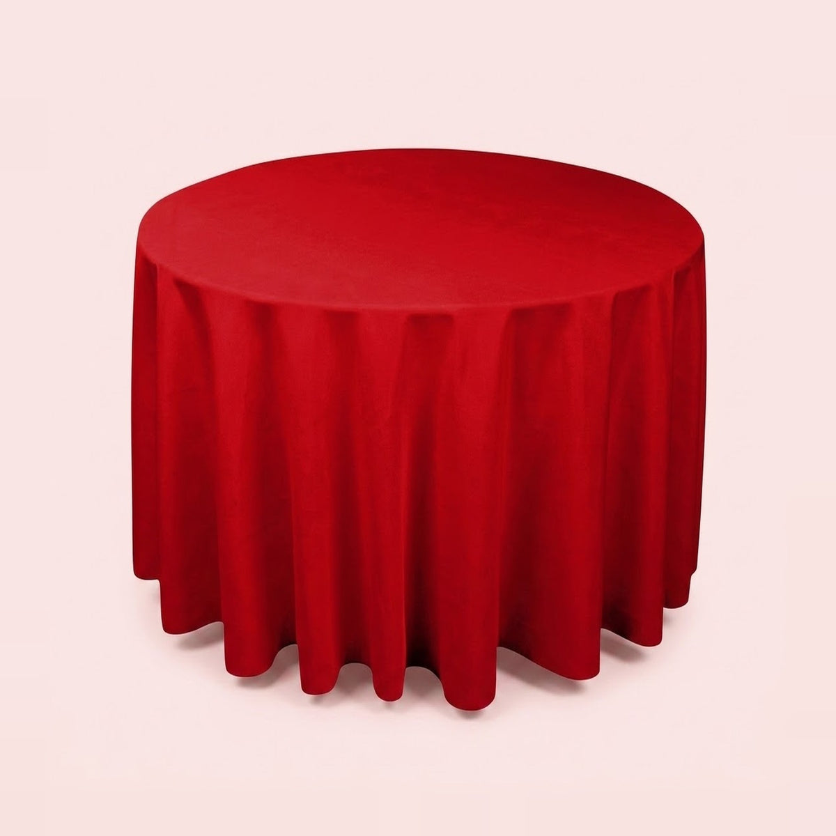 A round red tablecloth draped over a round table, shown against a solid pale pink background.