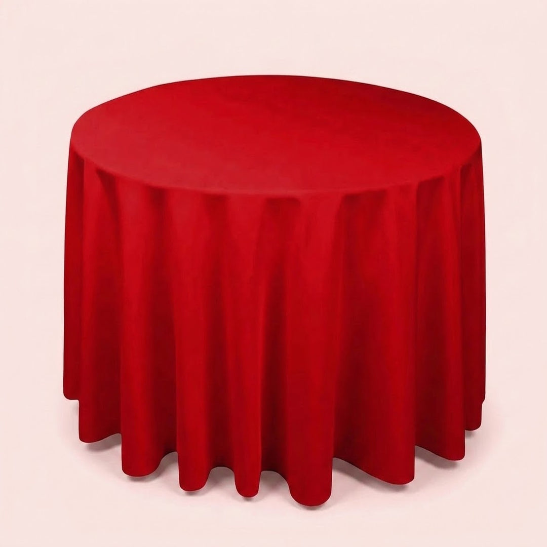 A round red tablecloth draped over a round table, shown against a plain light pink background.