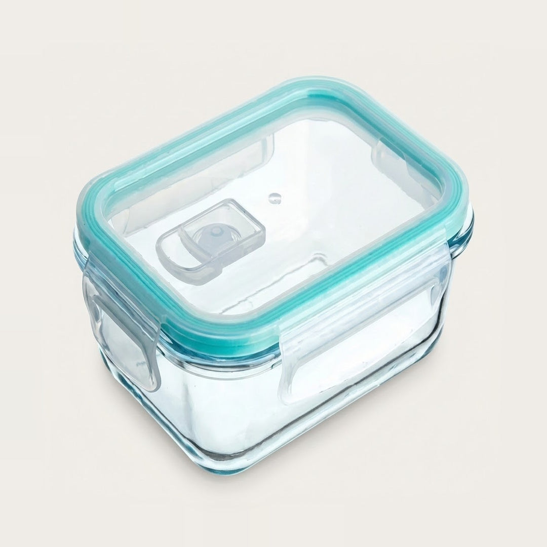 A square glass food storage container with a clear lid and a light teal silicone seal, shown on a plain light beige background.