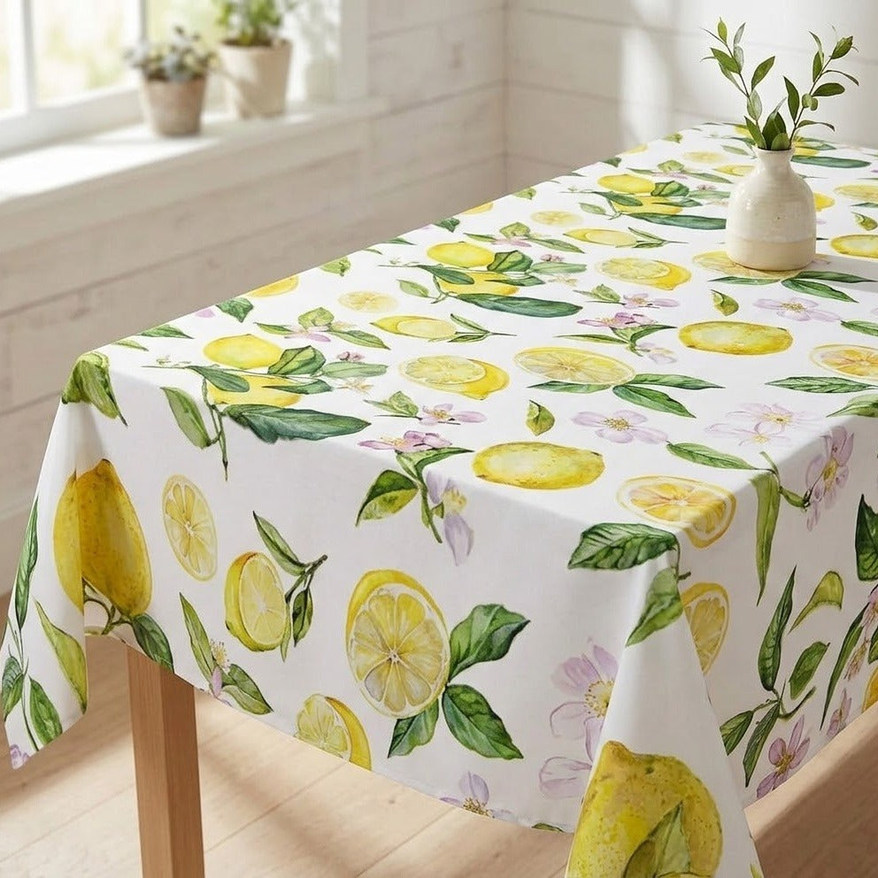 A white rectangular tablecloth with a vibrant watercolor lemon and flower print, draped over a wooden table in a bright, sunlit room.